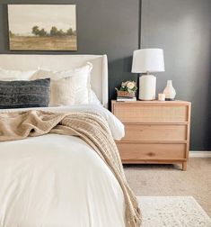 a bed with white linens and pillows in a gray room next to a dresser