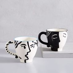 two black and white mugs with faces painted on them sitting next to each other