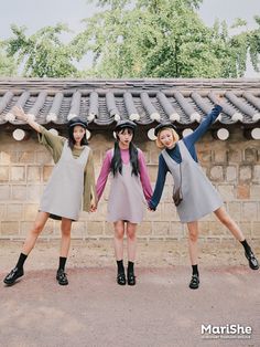 three young women standing next to each other in front of a brick wall and roof