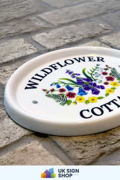 a white sign that says wildflower cottage on the side of a brick road with flowers painted on it