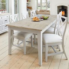 a dining room table with white chairs and a plate of food on the table in front of an open fire place