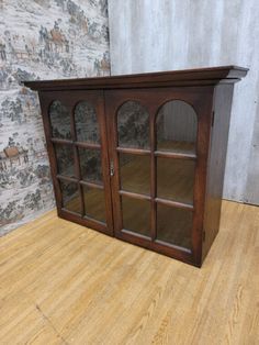 an old wooden cabinet with glass doors on the top and bottom, in front of a wallpapered background