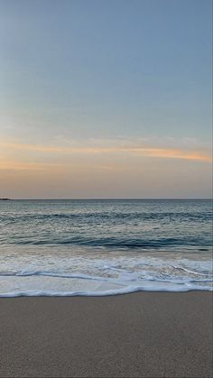 an empty beach with waves coming in to shore and the sun setting on the horizon