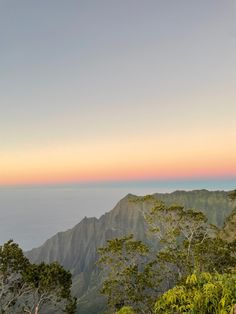 the mountains are covered in trees and plants as the sun is setting over the ocean