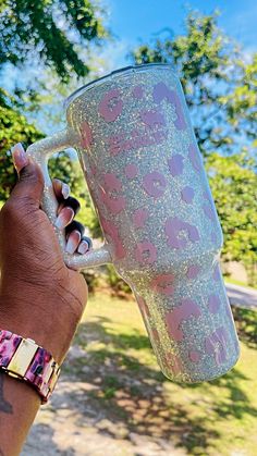 a person holding up a pink and white coffee cup in their left hand while wearing a bracelet