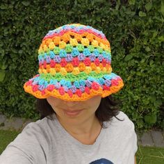 a woman wearing a multicolored crocheted sunhat in front of a hedge