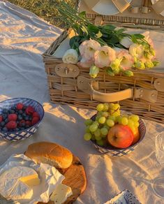 a picnic with bread, fruit and flowers on the table in front of an open wicker basket