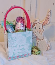 an easter basket filled with eggs and other items sitting on a bed next to a wooden bunny