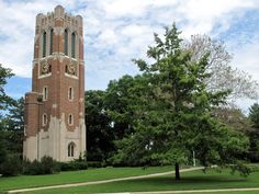 a tall brick clock tower sitting next to a lush green park filled with trees and grass