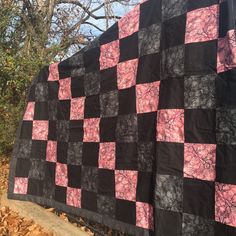 a black and pink quilt is hanging on a fence post in front of some trees