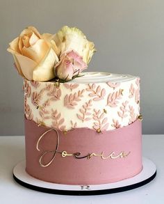 there is a pink and white cake with flowers on the top it has gold lettering