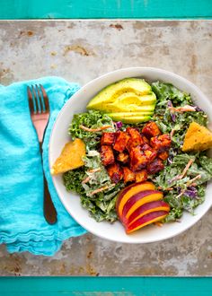 a white bowl filled with salad and fruit next to a fork on top of a blue towel