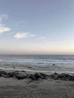 there is a bench on the beach by the water's edge with rocks in front of it