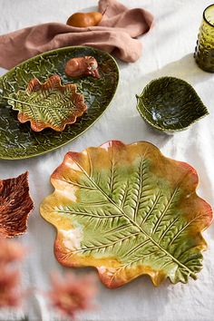 green and yellow leaf shaped dishes on a white table cloth next to two candles, an orange candle holder and some leaves