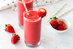 two glasses filled with strawberry smoothie next to strawberries