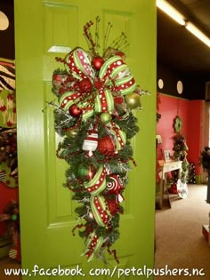 a green door decorated with red and white christmas wreaths, ornaments and ribbons on it