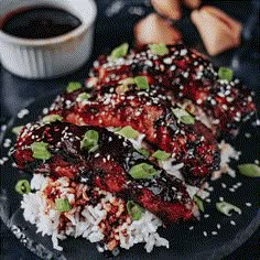 two pieces of meat with sauce and rice on a plate