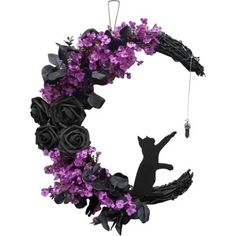 a black cat sitting on top of a purple flowered wreath with an acorn hanging from it's side