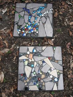 two pieces of mosaic tile sitting on the ground next to some leaves and grass,