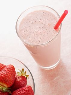 strawberries in a bowl next to a glass of milkshake on a table