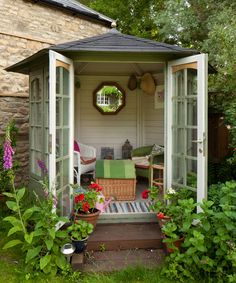 a garden shed with an open door and patio furniture in the back yard, surrounded by greenery