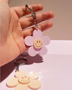 a hand holding a flower shaped keychain with two smiley faces attached to it