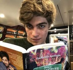 a young man is reading a book in a restaurant while looking at the camera with an intense look on his face