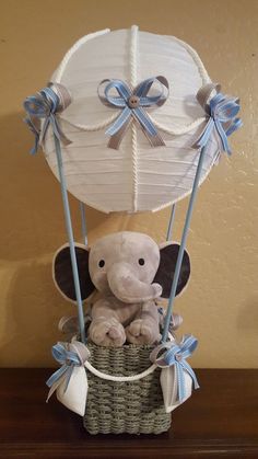 a stuffed elephant sitting in a basket with blue ribbon on the handle and an umbrella attached to it