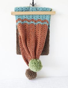 a crocheted blanket hanging on a wall with a pom - pom