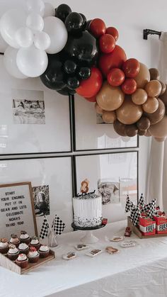 a table topped with lots of balloons and cupcakes next to a cake on top of a table