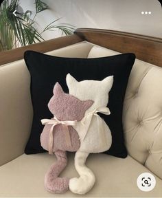 a pink and white cat pillow sitting on top of a couch next to a black pillow