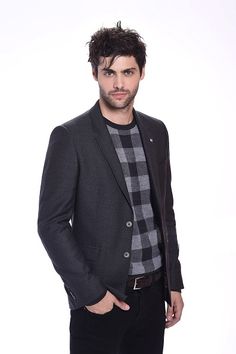 a man in a black jacket and plaid shirt posing with his hands in his pockets