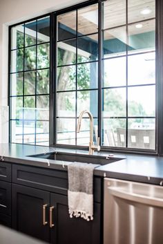 a kitchen with black cabinets and an open window that looks out onto the yard outside