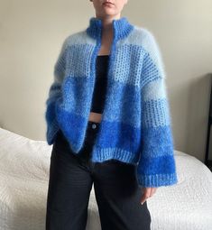 a woman standing in front of a bed wearing a blue and white knitted jacket