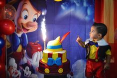 a young boy standing in front of a mickey mouse cake with lit candles on it