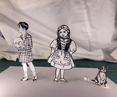 two paper cutouts of people standing next to each other with a dog sitting on the floor