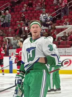 a hockey player standing on the ice with his arms around his chest and wearing green pants