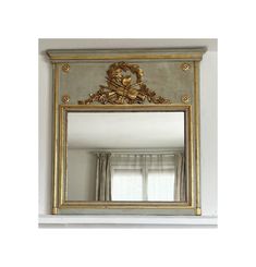 an ornate gold framed mirror hanging on the wall above a window in a white room