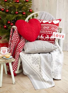 a white chair with red and white pillows on it next to a small christmas tree