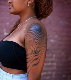 a woman with a tattoo on her arm and shoulder is standing in front of a brick wall