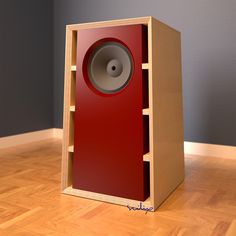 a red speaker sitting on top of a wooden floor in front of a gray wall