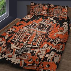 an orange and black bed spread with halloween themed designs on it, in front of a window