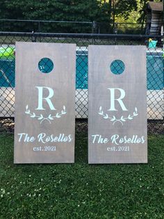 two personalized cornhole toss game boards on the grass in front of a fence