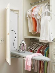 an ironing board and clothes hanging on a rail in a closet with white drawers