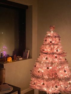 a pink christmas tree in a living room next to a window with the lights on