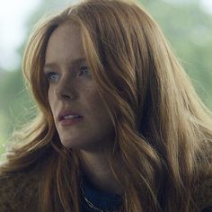 a woman with long red hair looking off into the distance