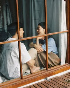 two people are sitting on the window sill looking at each other and laughing together