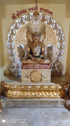 the golden buddha statue is in front of a white wall with red lettering on it