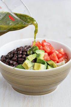 a bowl filled with black beans, avocado and tomatoes being drizzled over it