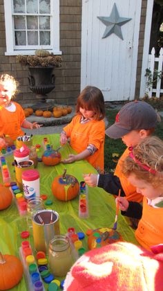 children in orange shirts sitting at a table with pumpkins on it and paint cans